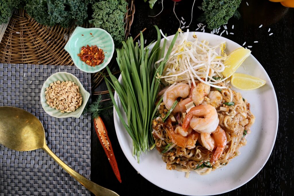 A colorful plate of Thai street food, featuring pad Thai with lime, chili flakes, and peanuts, showcasing traditional Thai flavors.