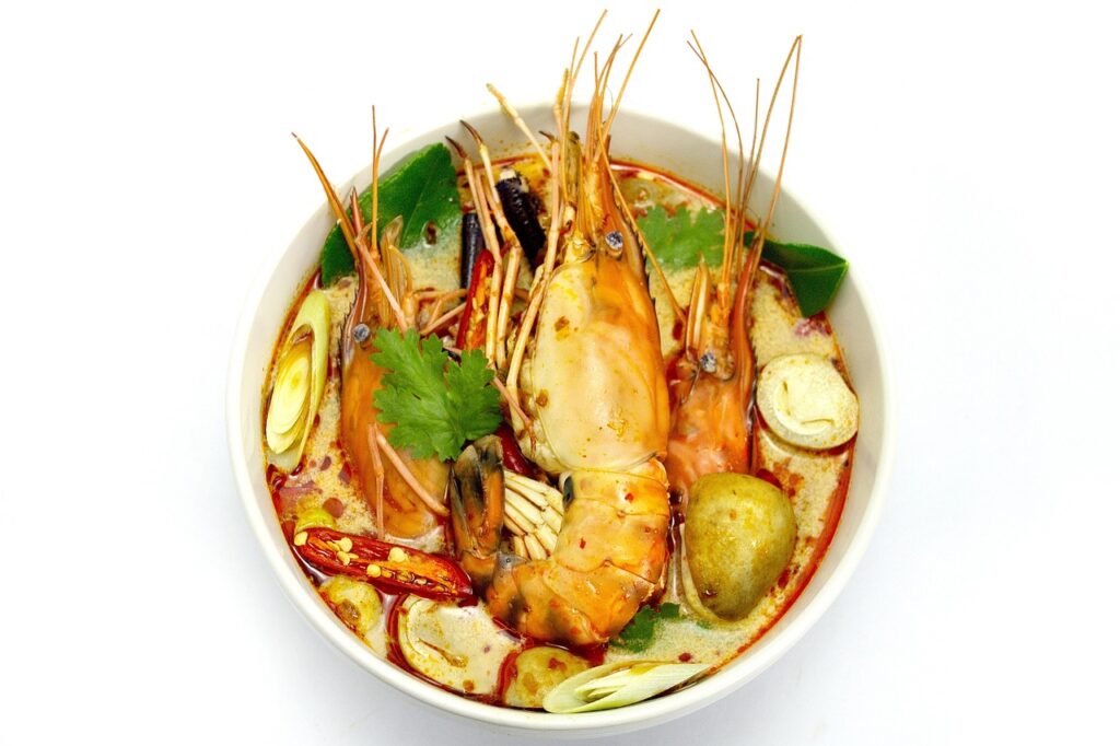 A bowl of Thai tom yum soup, featuring vibrant orange broth, shrimp, mushrooms, lemongrass, and lime, highlighting its spicy and sour flavors.